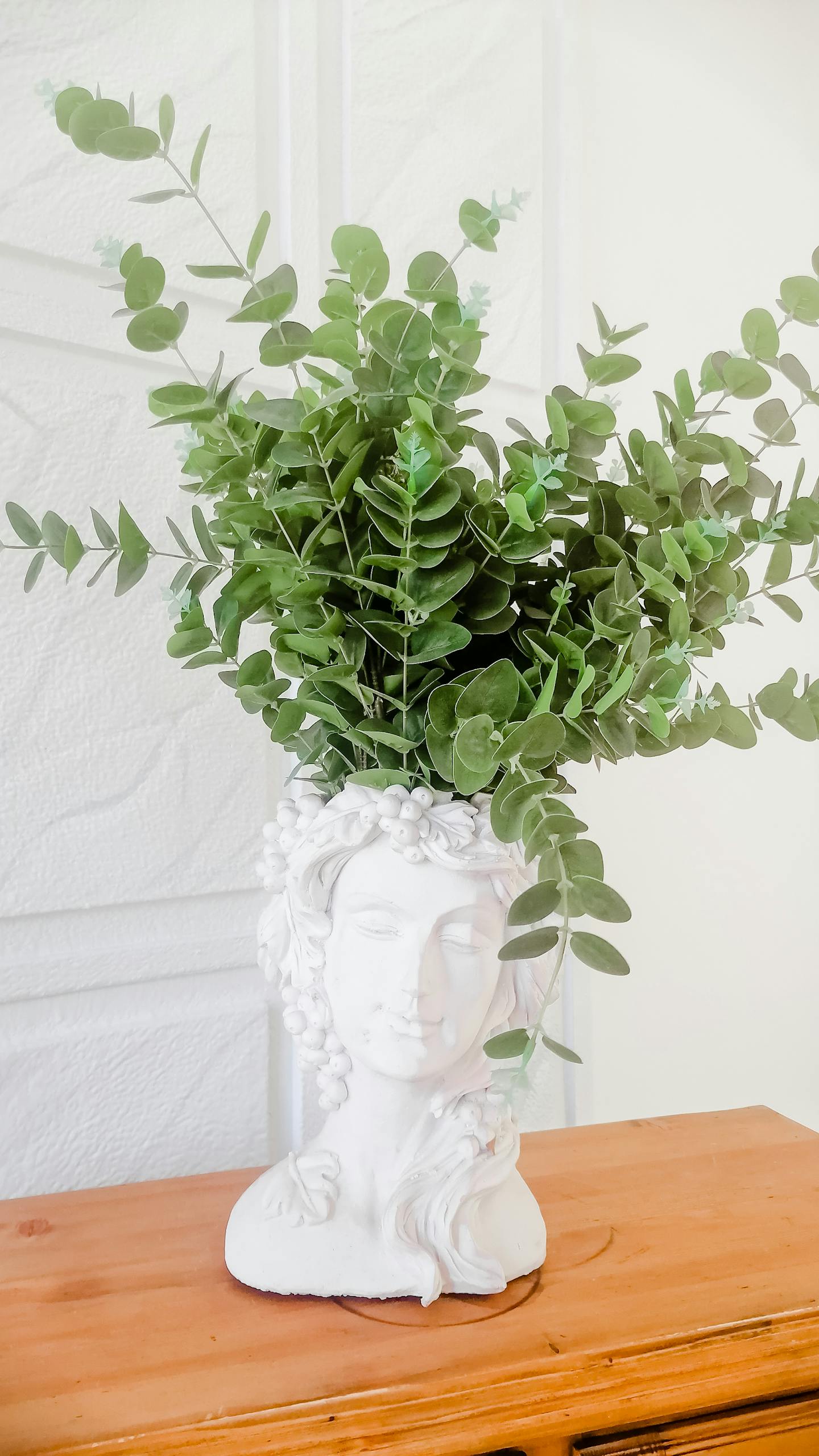 White sculpture vase with green foliage on a wooden surface. Perfect for home decor inspiration.