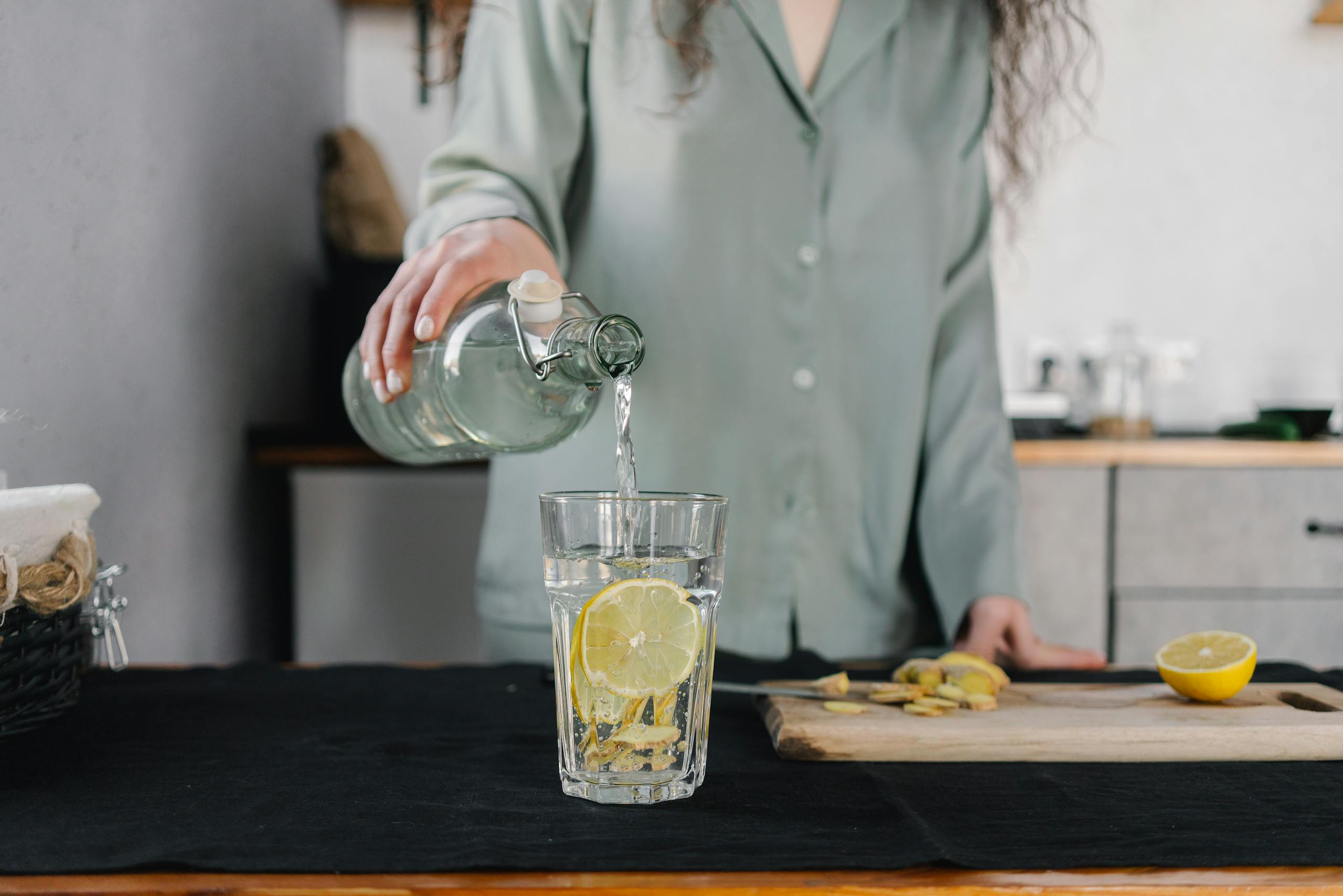 Woman pours water for lemon ginger infusion, promoting health and hydration.